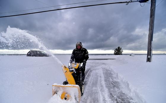 A man uses a yellow snowblower to clear snow. 