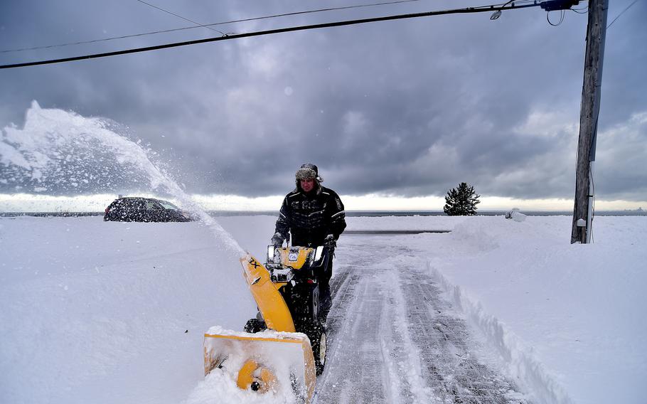 A man uses a yellow snowblower to clear snow.