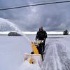 A man uses a yellow snowblower to clear snow. 