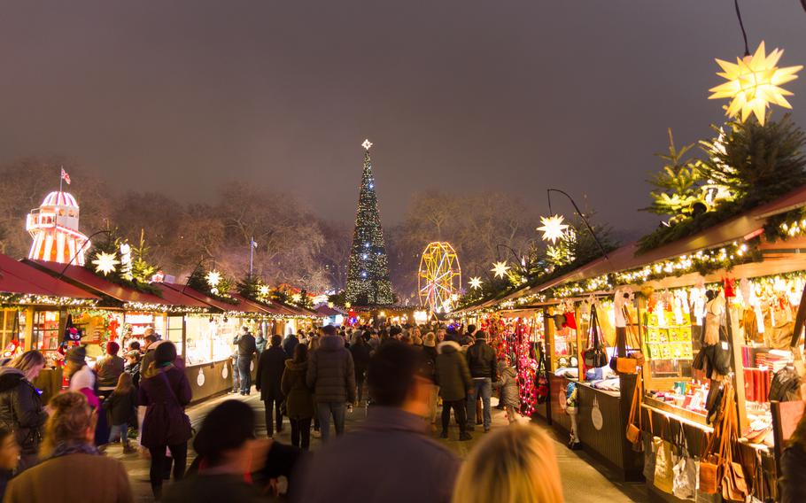 Brightly lit market stalls lead to a Christmas tree in the far distance.