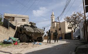 Two soldiers stand next to an armored vehicle on an empty street.