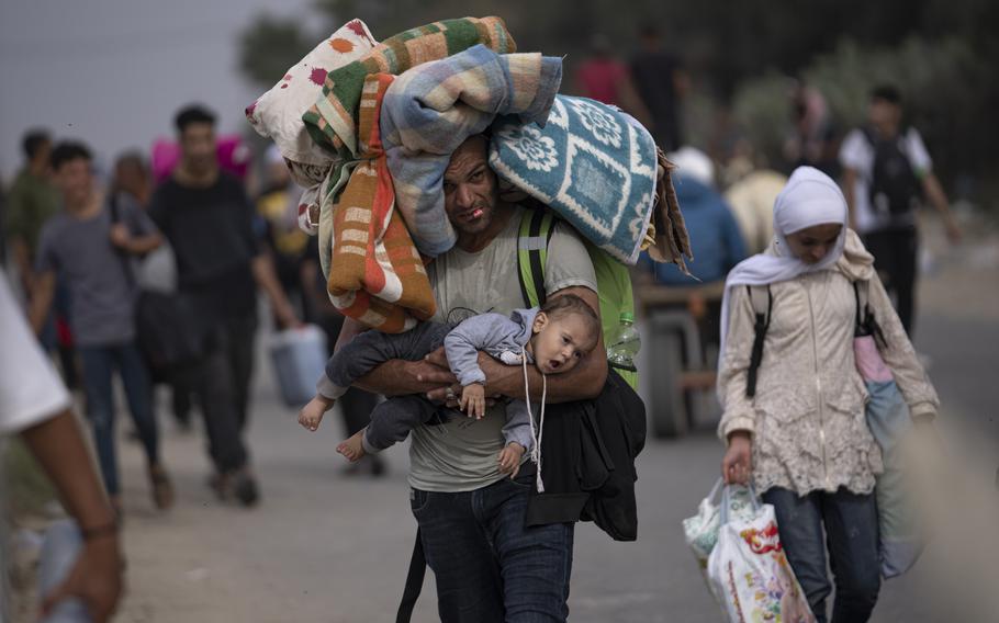 A man laden by a backpack and bedding also carries a baby in his arms as he walks down the road.