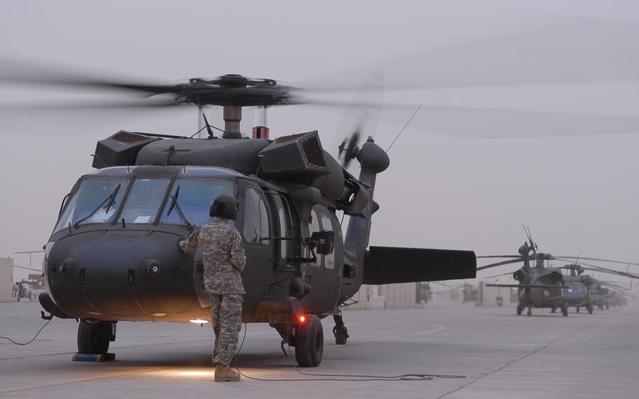 A soldier in camouflage uniform and black helmet stands next to a helicopter on a tarmac.