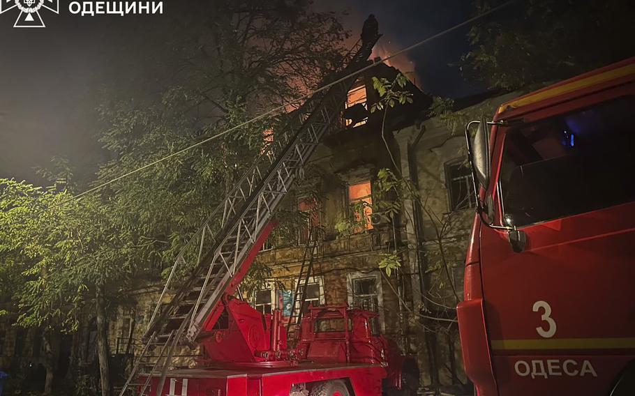 A fire engine with the ladder extended with the glow of a fire in the background. 