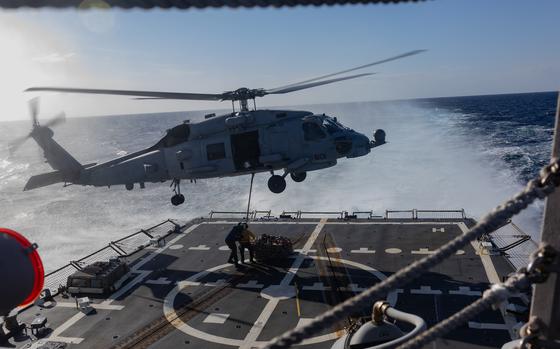  A MH-60R Sea Hawk helicopter hovers above a pair of sailors attaching a cargo hook.