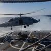  A MH-60R Sea Hawk helicopter hovers above a pair of sailors attaching a cargo hook.