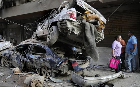 A Lebanese woman passes next of destroyed cars at the site of Thursday's Israeli airstrike, in Beirut, Lebanon, Friday, Oct. 11, 2024. (AP Photo/Hussein Malla)