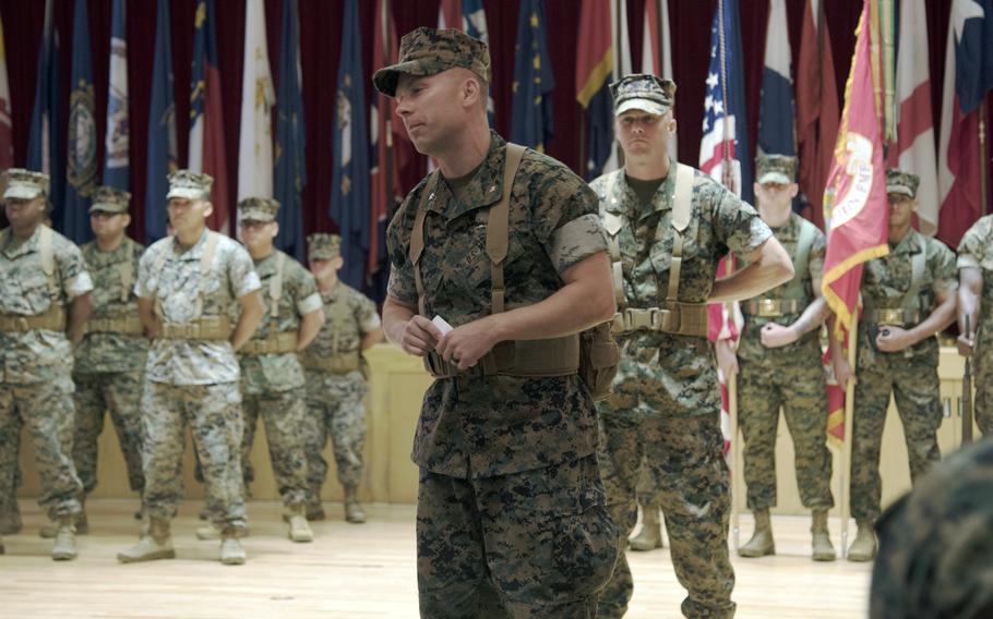 A Marine Corps officer speaks in front of a group of Marines standing at attention.