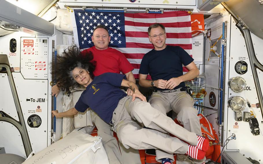 Three astronauts float in front of a U.S. flag aboard the International Space Station.