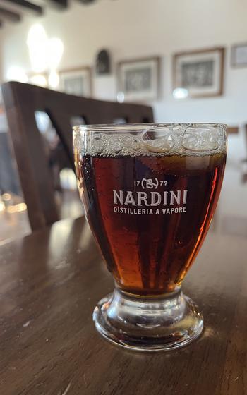 A brown, slightly frothy alcoholic drink in a Nardini Distillery glass sits on a table.