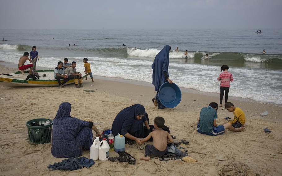 Women watch children and sit on the sand at the beach with jugs of cleaner and large laundry baskets.