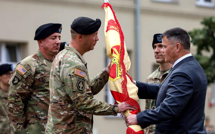 Col. Jesse Chace, incoming commander of U.S. Army Garrison Poland, takes the unit's guidon from Tommy Mize, right, Installation Management Command Europe director, during the garrison’s change of command ceremony at Camp Kosciuszko in Poznan, Poland, on June 28, 2024.