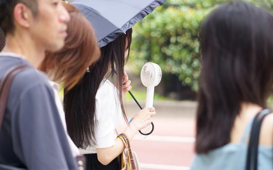 A woman uses a portable electric fan and a parasol to combat heat in Tokyo's Shinjuku ward, Wednesday, July 31, 2024. 