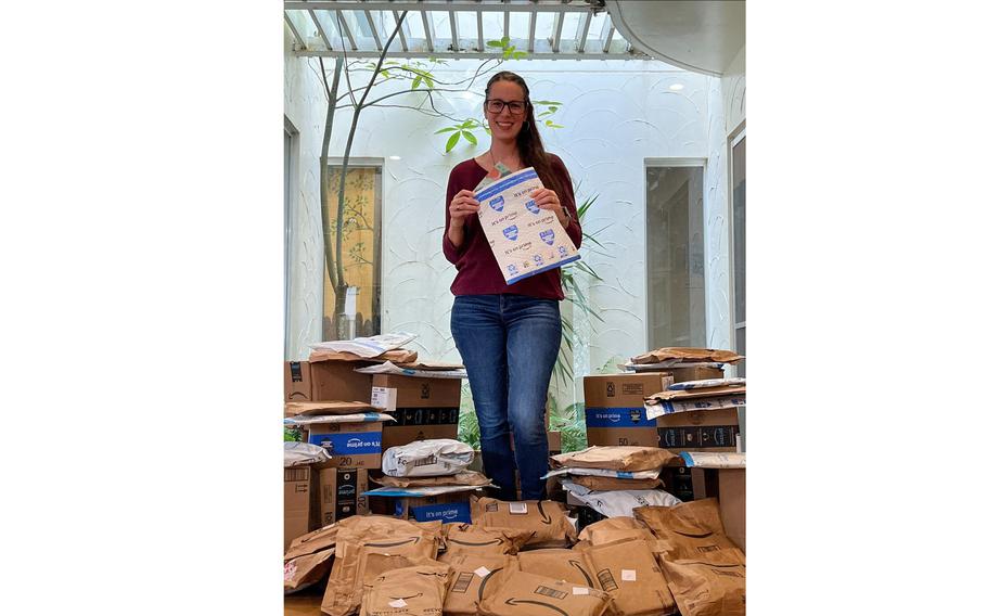 Caitlyn Webber stands, holding a packing envelope, with dozens of packages containing books at her feet.