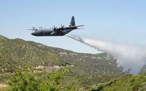 A U.S. Air National Guard MAFFS (Modular Airborne Fire Fighting System) equipped C-130J Super Hercules assigned to the 115th Airlift Squadron discharges a line of water simulating a fire retardant drop during aerial wildfire suppression training with the U.S. Forest Service and the California Department of Forestry and Fire Protection (CAL FIRE) in the mountains of the Angeles Forest above Santa Clarita, California, May 12, 2023. This week's training will culminate the second iteration of MAFFS training and celebrate a 50-year interagency partnership between the Department of Defense and the USDA Forest Service. The recertification training includes classroom sessions, flying and ground operations for Air Force aircrews, civilian lead plane pilots, and support personnel from the Forest Service, Bureau of Land Management, and other federal and state agencies. (U.S. Air National Guard Photo by Staff. Sgt. Michelle Ulber)