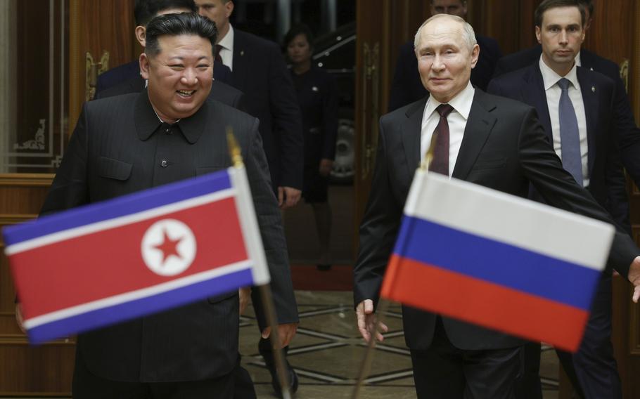 Vladimir Putin and Kim Jong Un stand behind Russian and North Korean flags.