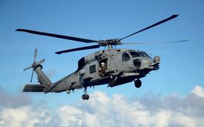 A helicopter descends to land on an aircraft carrier with the sea and clouds in the background.