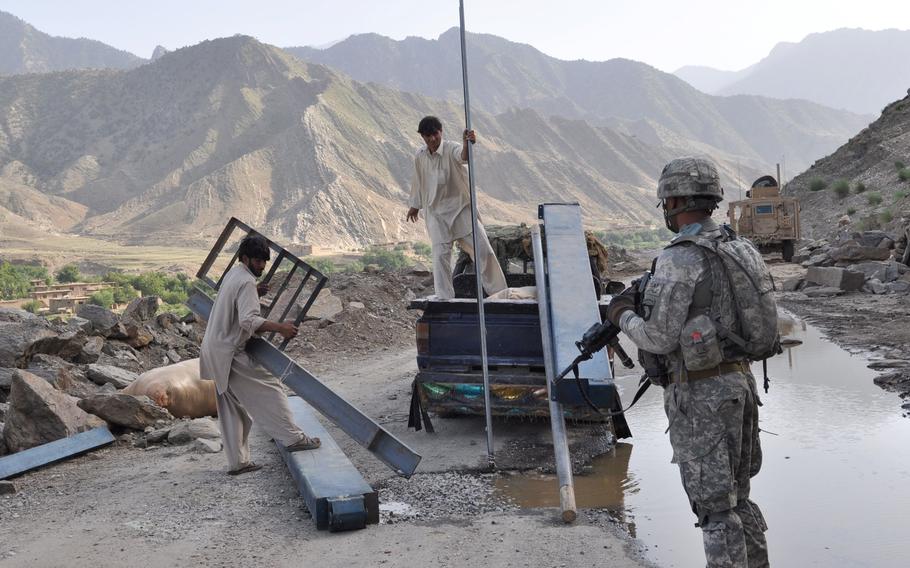 A soldier with the 327th Infantry Regiment watches as locals unload a delivery of building supplies to a home along the Pech River in Qandaro Village on July 16, 2010.