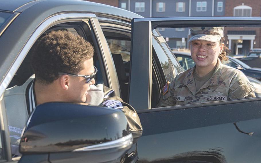 A soldier gets into the back seat of a vehicle as the driver looks out the window at her.