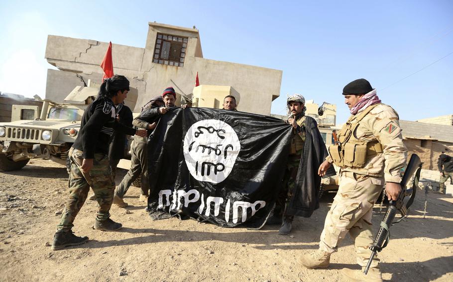 Iraqi Army soldiers celebrate as they hold a flag of the Islamic State group they captured during a military operation to regain control of a village outside Mosul, Iraq, Nov. 29, 2016. Ten years after the Islamic State group declared its caliphate in large parts of Iraq and Syria, the extremists now control no land, have lost many prominent founding leaders and are mostly away from the world news headlines. 