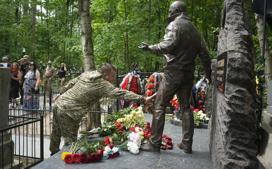 FILE - A fighter of the Wagner private military force touches a sculpture of Russian mercenary chief Yevgeny Prigozhin at his grave at the Porokhovskoye Cemetery in St. Petersburg, Russia, on Saturday, June 1, 2024. Prigozhin died in a suspicious air crash on Aug. 23, 2023, two months after launching a brief armed rebellion against the Russian military leadership. (AP Photo/Dmitri Lovetsky, File)