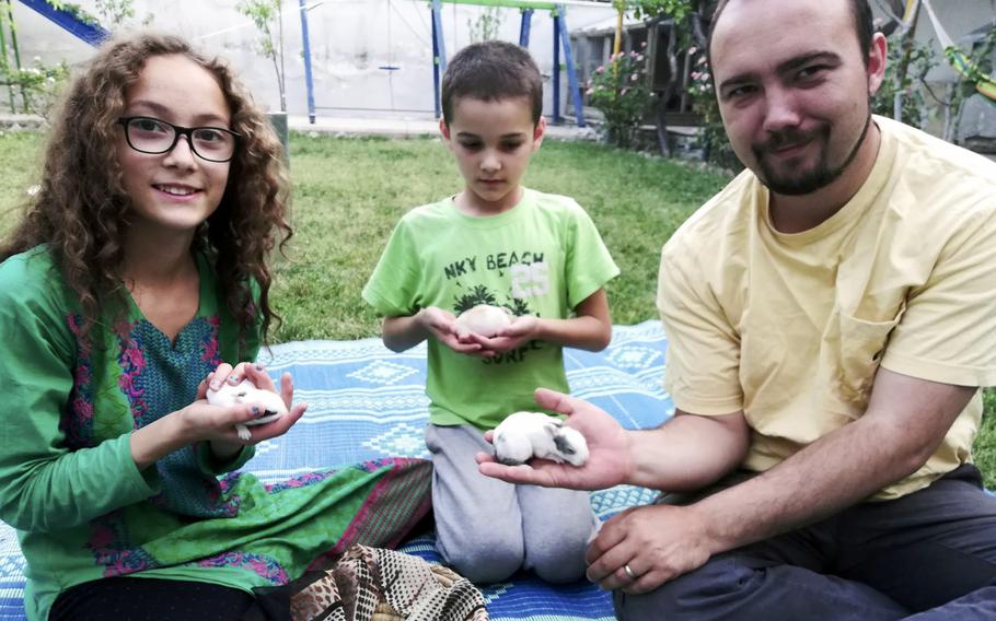 A man and his two children sit on the floor and hold baby rabbits in their hands.