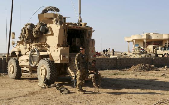 Two soldiers by an armored vehicle, one standing and the other sitting.