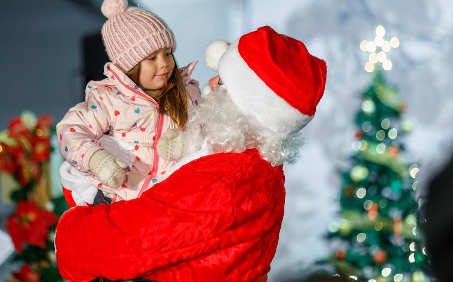 A young girl with a pink hat smiles at Santa.