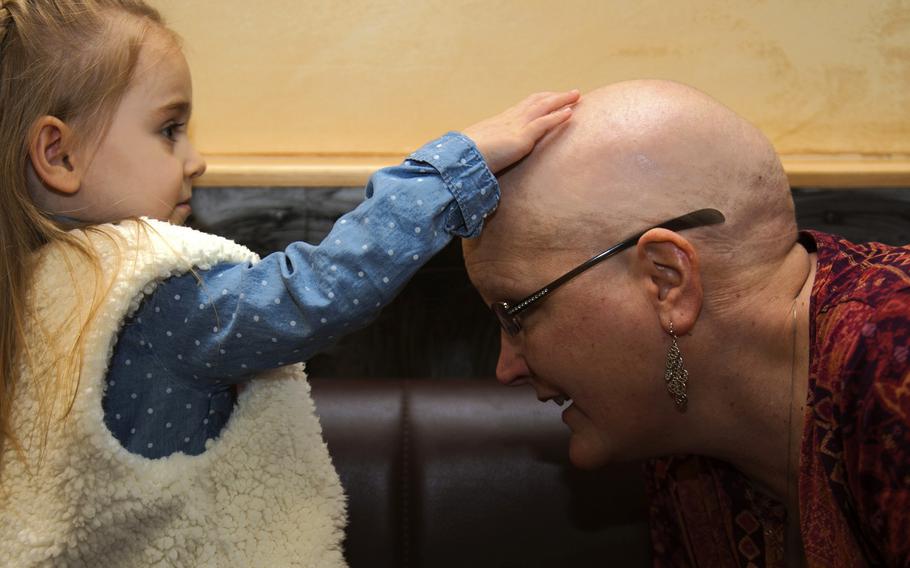 Theresa Lukens, right, breast cancer patient and wife of Chief Master Sgt. Richard Lukens, 52nd Maintenance Group chief enlisted manager, lets a friend’s daughter feel her head during lunch at Spangdahlem Air Base, Germany, Feb. 7, 2017. Lukens undergoes chemotherapy, a cancer treatment which can create a number of side effects to include fatigue, nausea, mouth and throat problems, skin and nail changes, easy bruising and bleeding, infection and hair loss.