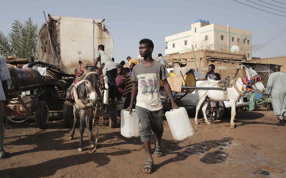 A Sudanese man carries buckets of water next to a donkey