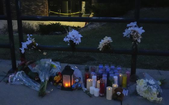 Flowers and candles sit on a sidewalk by a railing to honor two people killed in a school shooting.