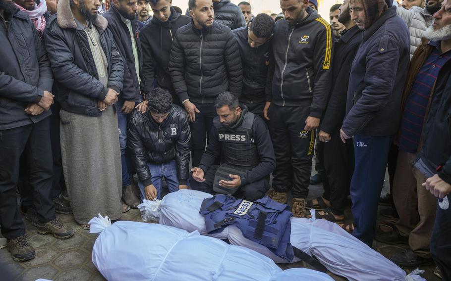 People surround bodies wrapped in white body bags.