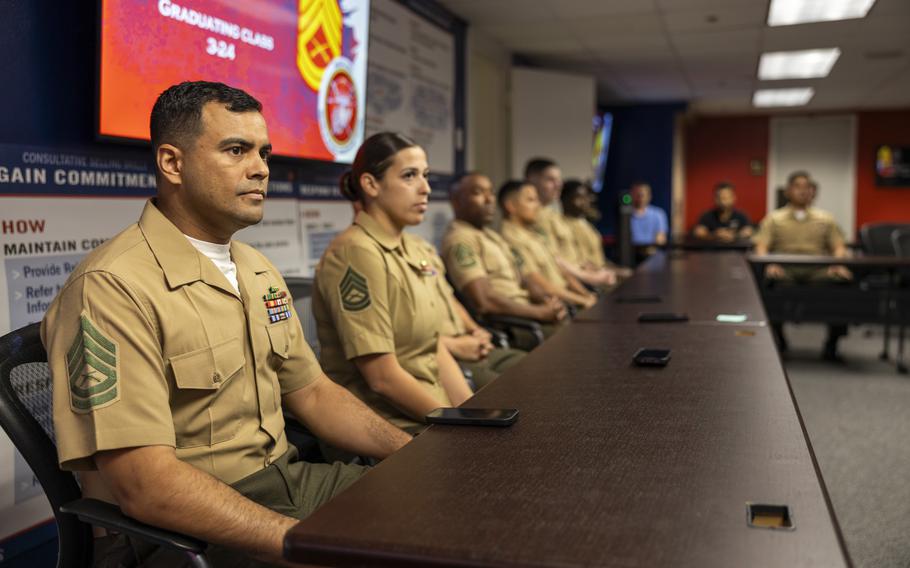 Marines sit at a table with a sign on a screen in the background that says “Graduating Class 324.”