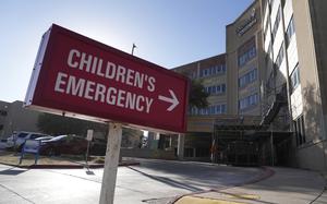 A red sign outside of a hospital reads “Children’s Emergency” with an arrow pointing to the right.