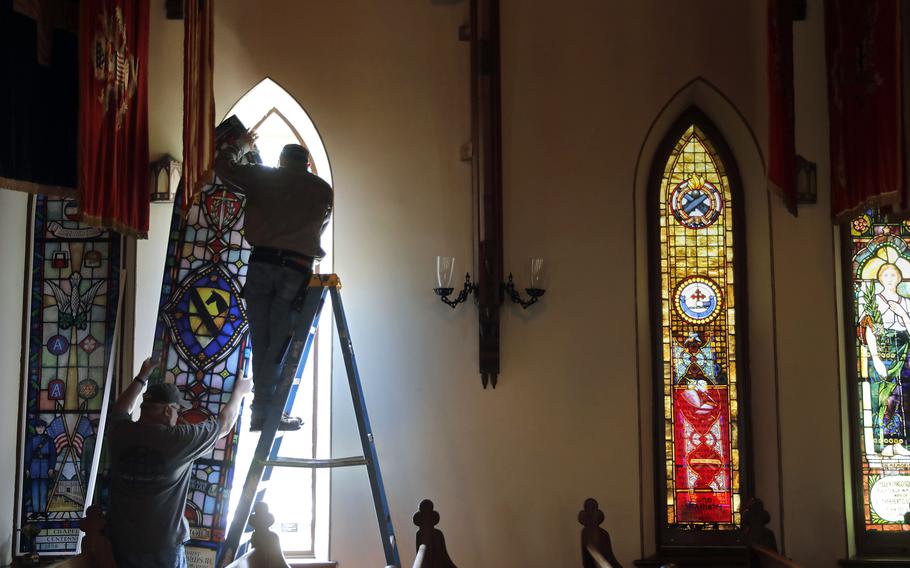 Jeff Speake, left, and Troy Kidd of Lynchburg Stained Glass install a temporary window on the Chapel of the Centurion on Fort Monroe on June 15, 2021. Eight stained glass windows of the chapel are being removed and restored as part of a wide scale project to overhaul the oldest continually used wooden military house of worship that opened in 1856.