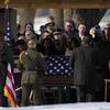 People mourn in front of a casket draped with the American flag.