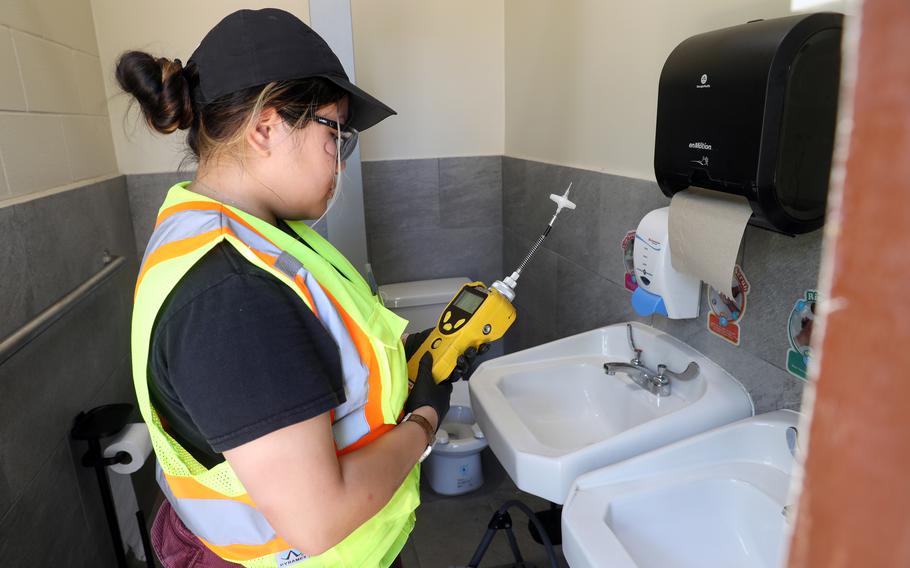 A woman wearing a reflective vest holds a water testing device in front of a bathroom sink.