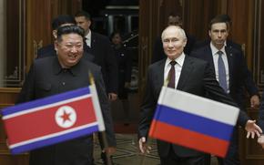 Russian president Vladimir Putin and North Korean leader Kim Jong Un stand beside each other with their respective flags in the foreground.