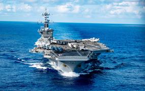 A U.S. aircraft carrier, seen from above, sails on the open ocean.