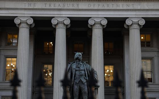 A statue stands in front of the columned facade of the Treasury Department building.