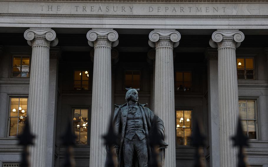 A statue stands in front of the columned facade of the Treasury Department building.