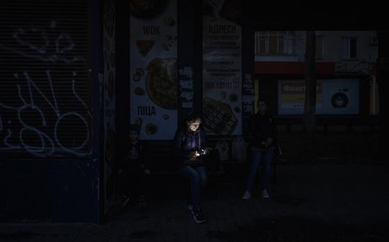 A woman looks at her phone while sitting in near-darkness in Kherson, Ukraine.