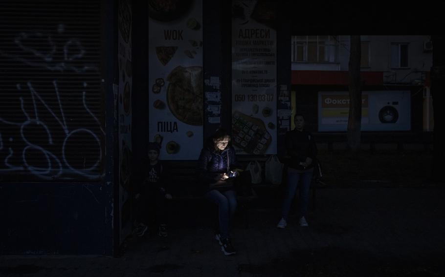 A woman looks at her phone while sitting in near-darkness in Kherson, Ukraine.