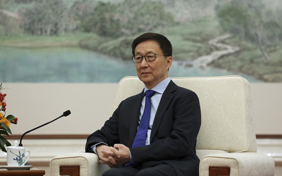 A man in glasses and a suit sits in a white upholstered chair.