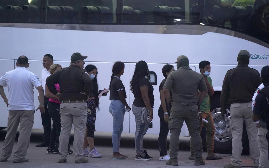 Migrants stand in line to board a bus 