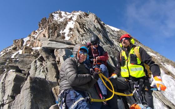 Nicolaus Marshall, left, Cathy Morth and an emergency responder wait for a helicopter to drop a cable to airlift Marshall, who was injured July 20, 2024, while climbing the Nadelhorn, a mountain in the Swiss Alps. The photo was taken by Malcolm Isbell, a U.S. Air Force civilian employee who taught mountaineering first aid at Ramsteain Air Base in Germany for four years.