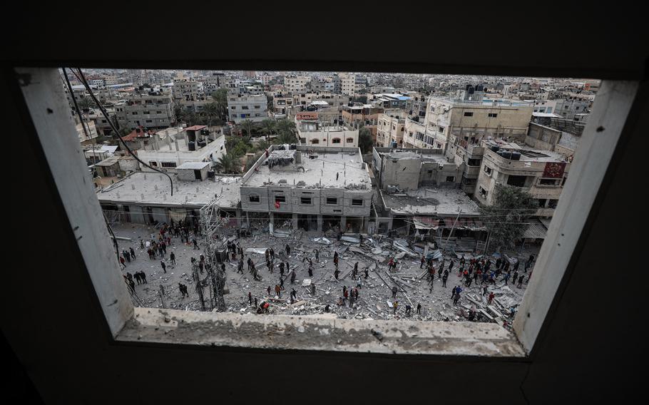 A long-range view through a window of people inspecting damage after an airstrike.