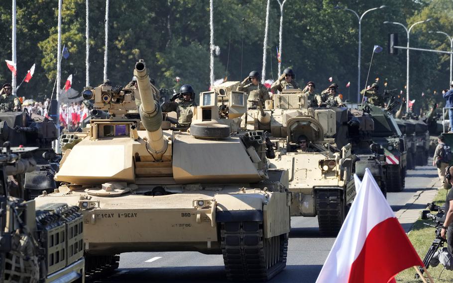 Abrams tanks parade down a street in Poland.