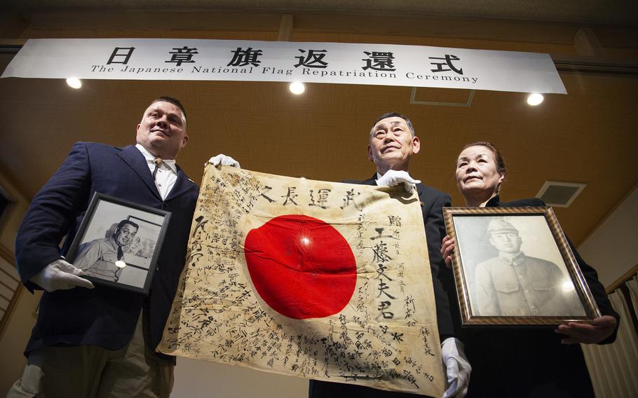 An American man poses with a signed Japanese flag held by a Japanese pair.