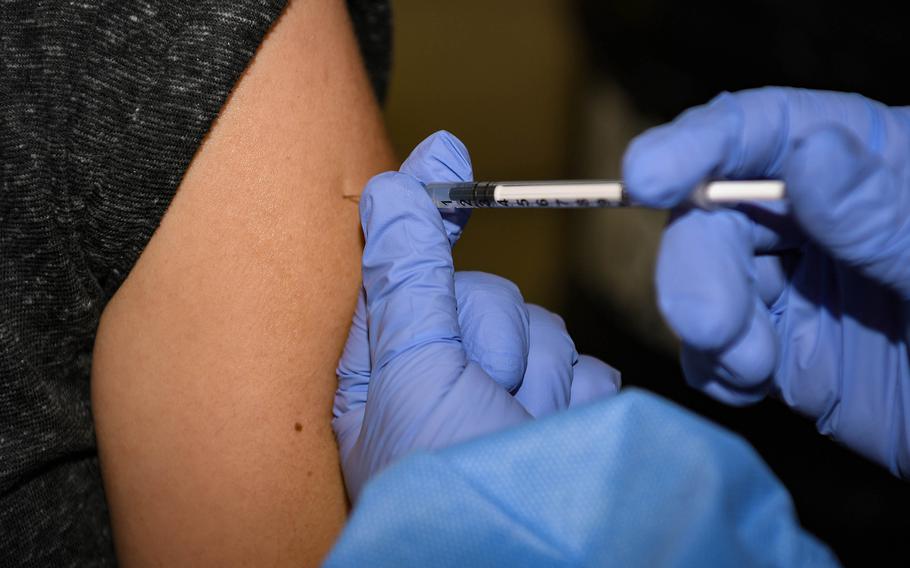 Two gloved hands injecting a vaccine into an arm.